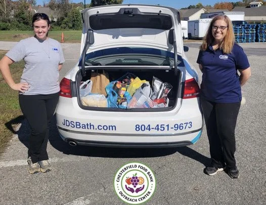 JDS Bath employees stand beside food bank car filled with canned goods