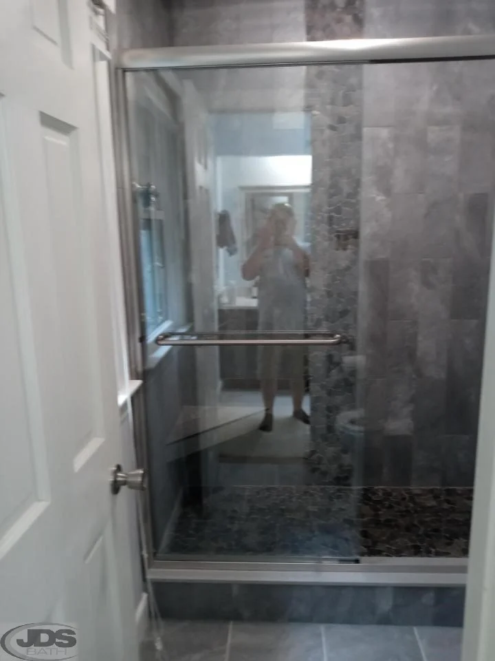 After photo of new shower with stone walls and closed glass doors.
