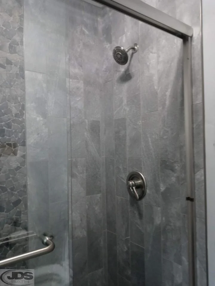 After photo of shower with stone walls and glass doors.