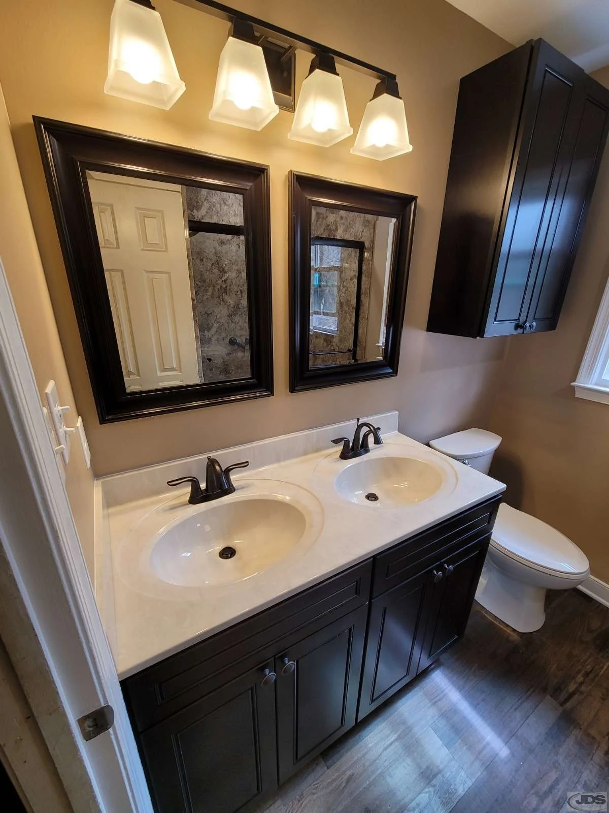 Dark wood double vanity with storage cabinet over the toilet