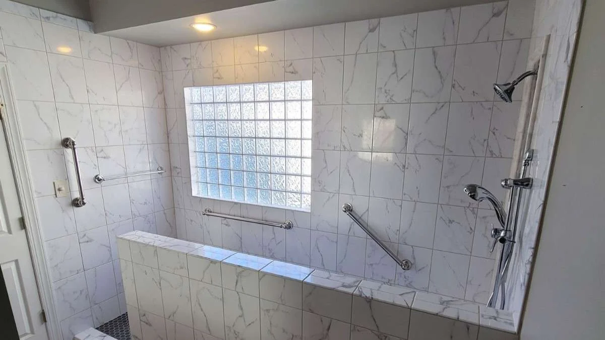 Accessible walk-in shower with beautiful white tile work and small frosted window