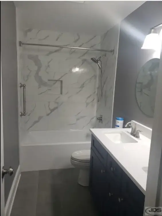 A newly installed white acrylic bathtub with tiled surround in a bright bathroom by JDS Bath.