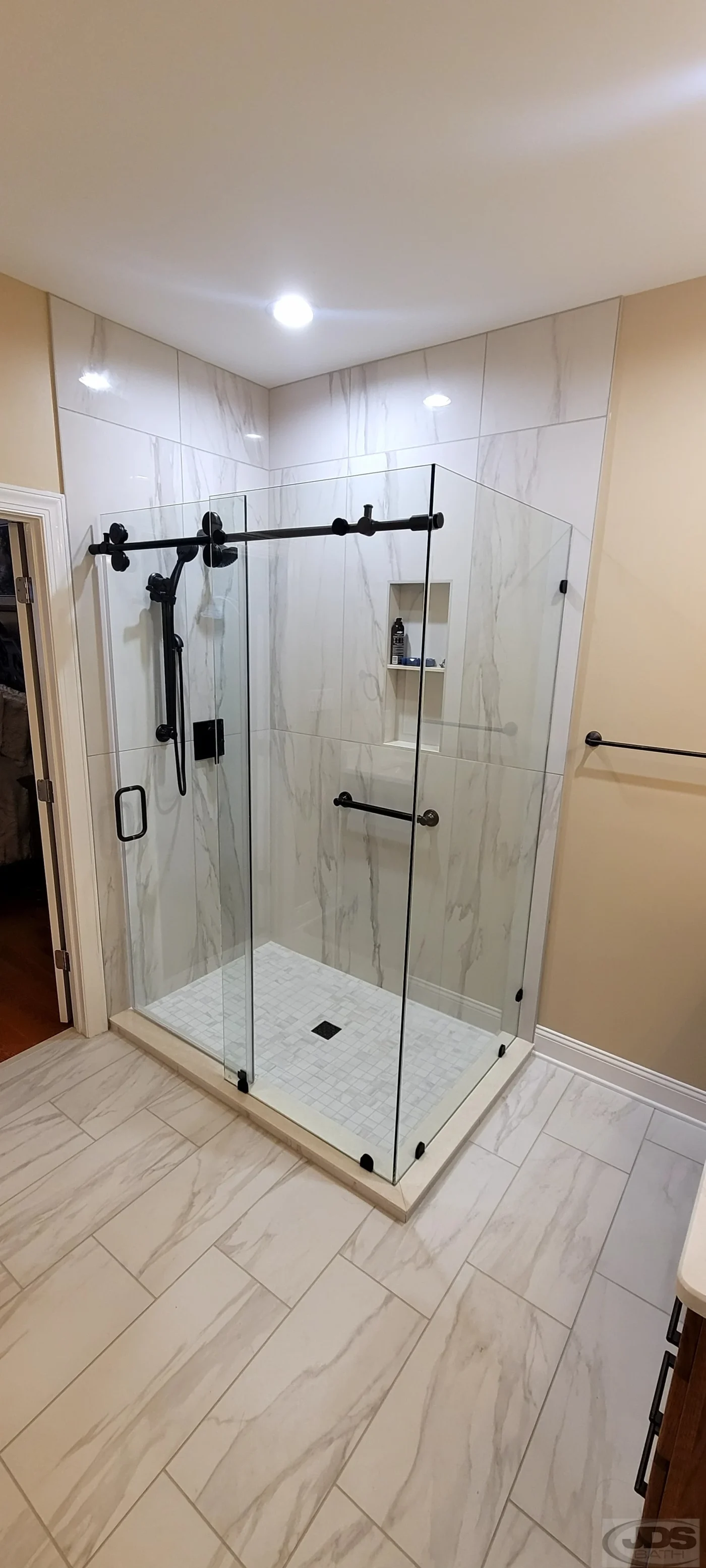 A finished shower with a glass door and clean grout lines in a remodeled bathroom by JDS Bath.