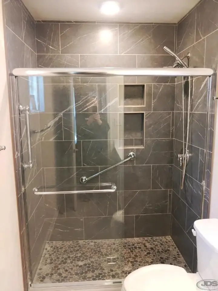 A newly installed tiled walk-in shower with a glass panel in a bright bathroom remodeled by JDS Bath.