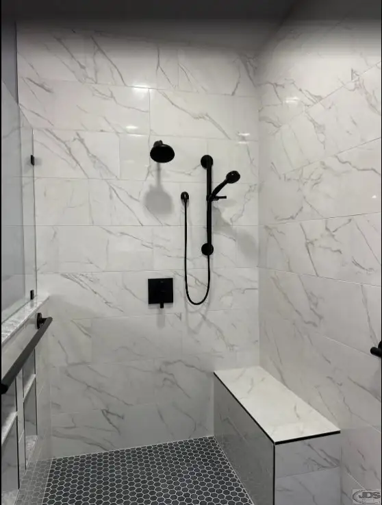 A walk-in shower with a bench seat and a handheld shower.